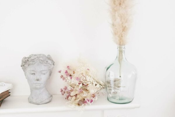 pot en pierre d'une tête de femme style Grèce antique avec des fleurs séchées blanches et roses